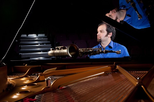 Jesse in blue shirt at the piano. Black background. 