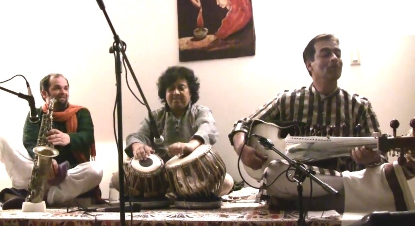 Jesse Bannister, Rajeeb Chakraborty and Subhen Chatterjee seated on the floor playing their instruments.