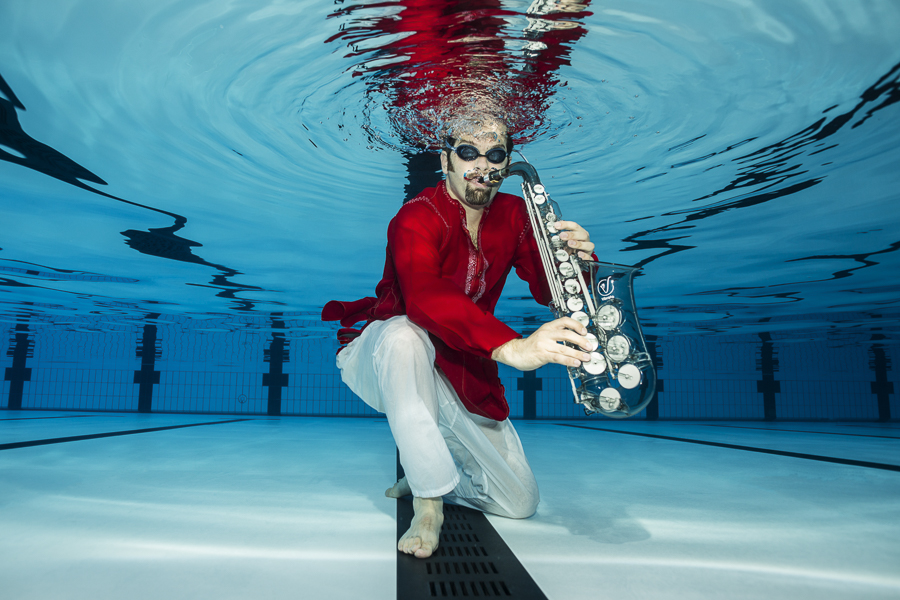 Jesse Bannister in red and white playing a glass saxophone with Maya Almeida in a multicoloured indian stitched top playing a blue ukelele. 