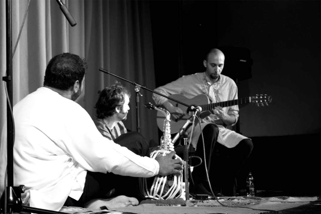 Black and white photo of Jesse and Bhupinder watching Guiliano playing his guitar from Dewsbury 2006 