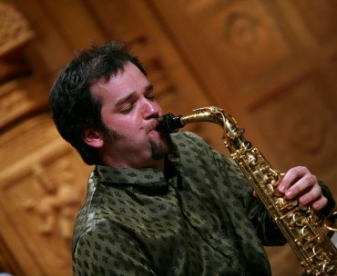 Jesse in a green shirt blowing his saxophone. 